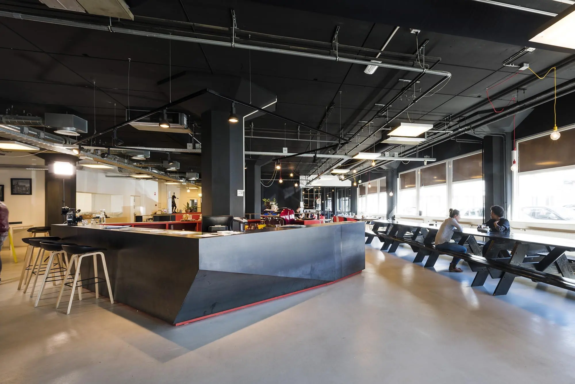 Moderne bedrijfsruimte aan de Anthony Fokkerweg met een centrale bar, industriële uitstraling en lange zitbanken bij de ramen.